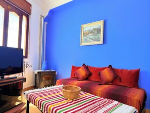 Ein Zimmer mit blauer Wand, einem Bett mit bunten Kissen, einem Fernseher, einem Holzschrank und einem Gemälde.