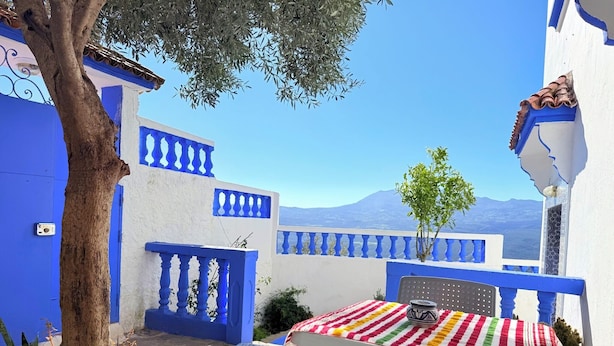Ein blau-weißes Gebäude mit Balkon, Blumentöpfen und einem Tisch mit gestreifter Tischdecke.