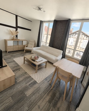 Ein modernes Wohnzimmer mit Sofa, Couchtisch, TV-Stand und einem großen Fenster mit Vorhängen.