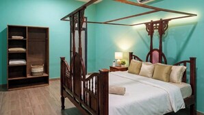 Una cama con dosel y estructura de madera, un ventilador de techo, un equipo de aire acondicionado y una mesita de noche con lámpara.