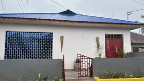 Un edificio de una sola planta con techo azul, puerta roja y ventana con diseño de cuadrícula.