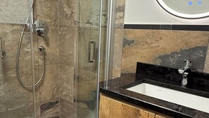 Moderni kylpyhuone, jossa on lasinen suihkuseinä, puinen allaskaappi ja suuri peili.