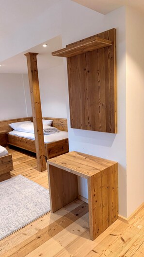 Ein Zimmer mit einem Holzbett, einem kleinen Holztisch und einem an der Wand befestigten Regal.