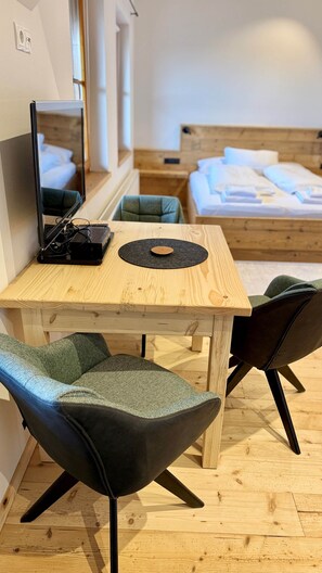 Ein Zimmer mit einem Holztisch, zwei Stühlen, einem Bett und einem Spiegel.