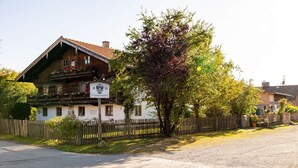 Un edificio de madera tradicional con balcón, un cartel con números y un jardín cercado.