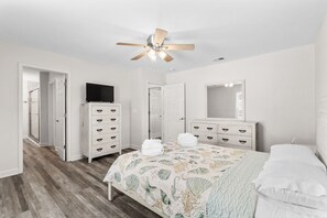 A bedroom with a bed, a ceiling fan, a dresser, a television, and a mirror. - "Coastal Belle" By Beach Star Near Marsh Walk (Murrells Inlet)