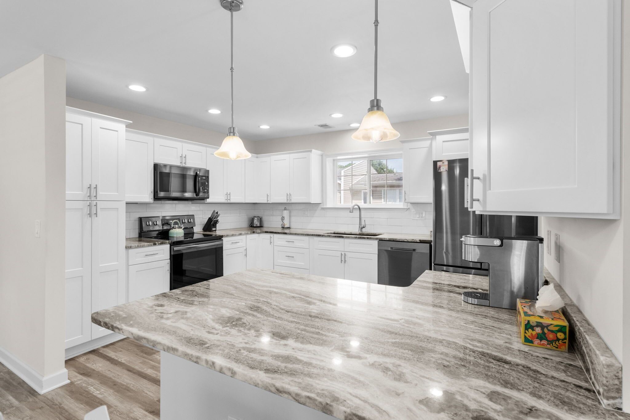 A modern kitchen with white cabinets, stainless steel appliances, and a marble countertop.