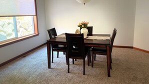 Een eetruimte met een houten tafel, stoelen, een vaas met bloemen en een hanglamp.