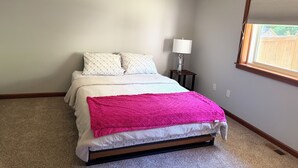 Een slaapkamer met een bed, een nachtkastje met een lamp, een raam met jaloezieën en een tapijtvloer.