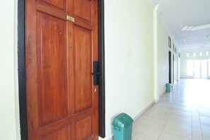 Un couloir avec une porte en bois portant l’inscription « 203 », une poubelle et un sol carrelé.