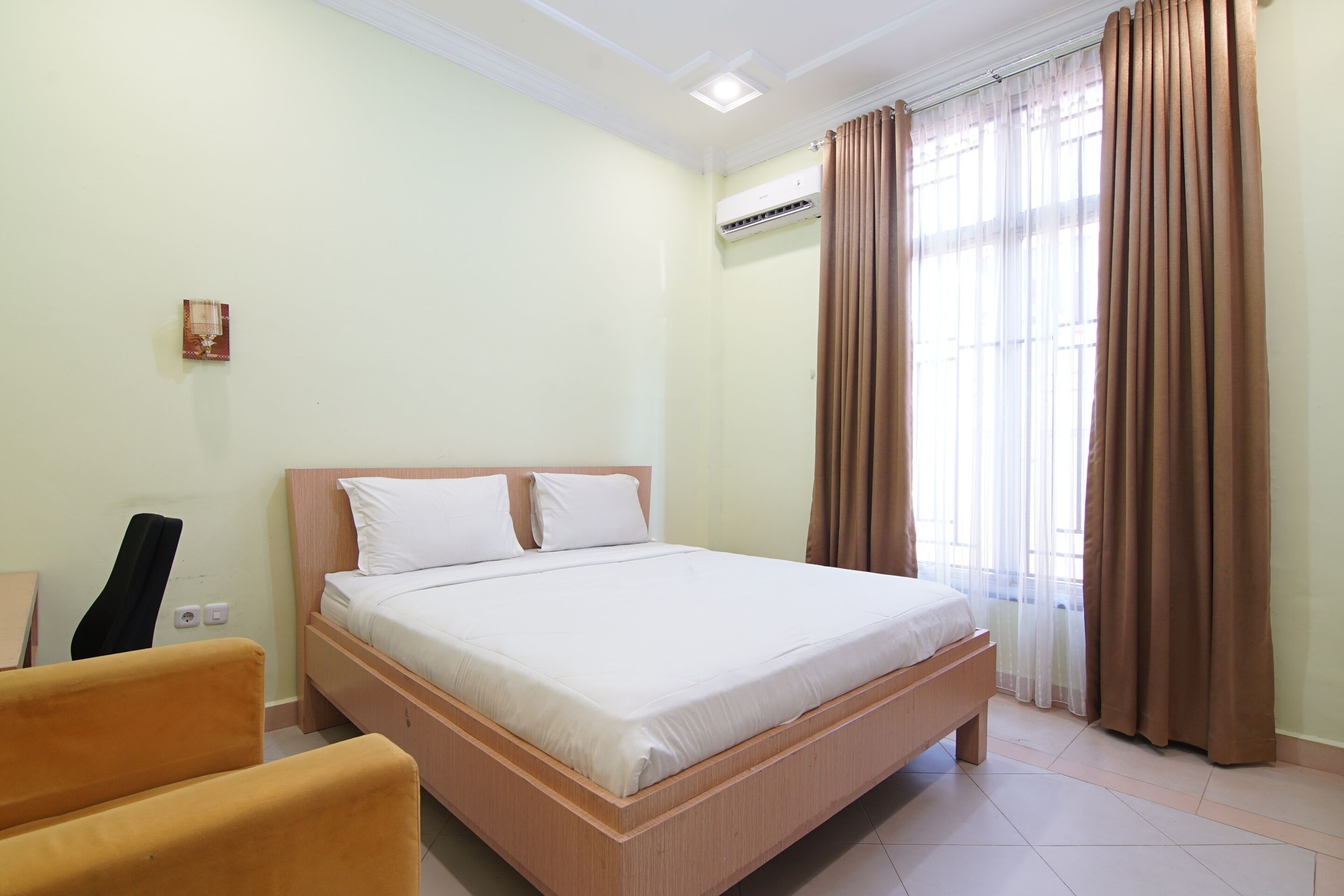Una habitación de hotel con una cama, una silla, un equipo de aire acondicionado y una ventana con cortinas.