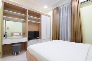 Una habitación de hotel con cama, televisor, escritorio con espejo y armario.