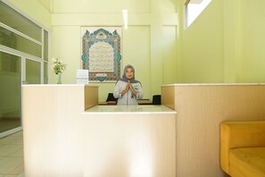 Ein Empfangstresen mit einem gerahmten Kalligraphiebild, einer Blumenvase und einem gelben Sofa.