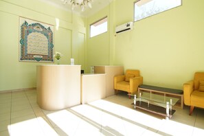 Un área de recepción con una mesa de recepción, dos sillones amarillos, una mesa con superficie de vidrio y un equipo de aire acondicionado instalado en la pared.