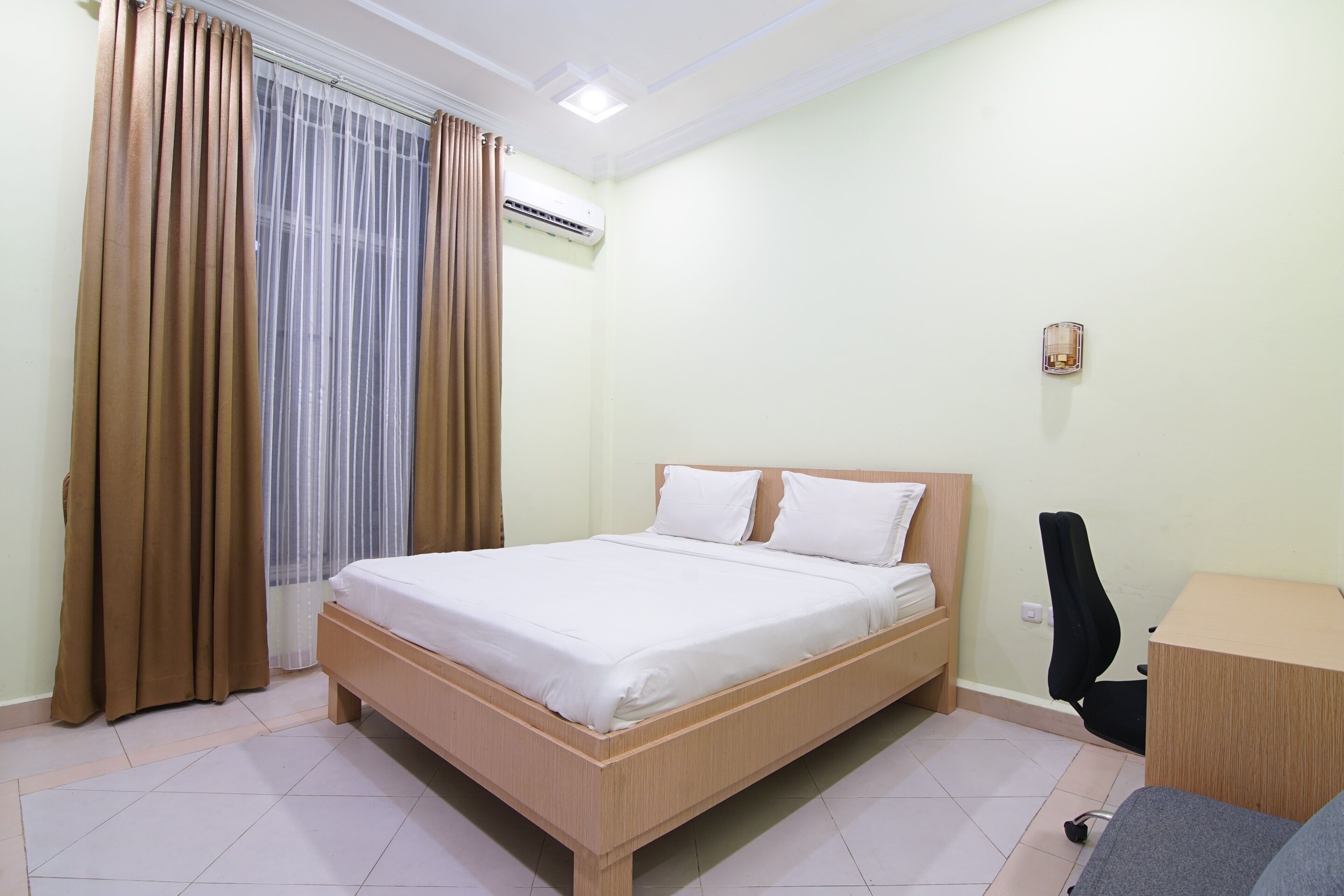 Un dormitorio con cama, cortinas, aire acondicionado, escritorio y una silla.