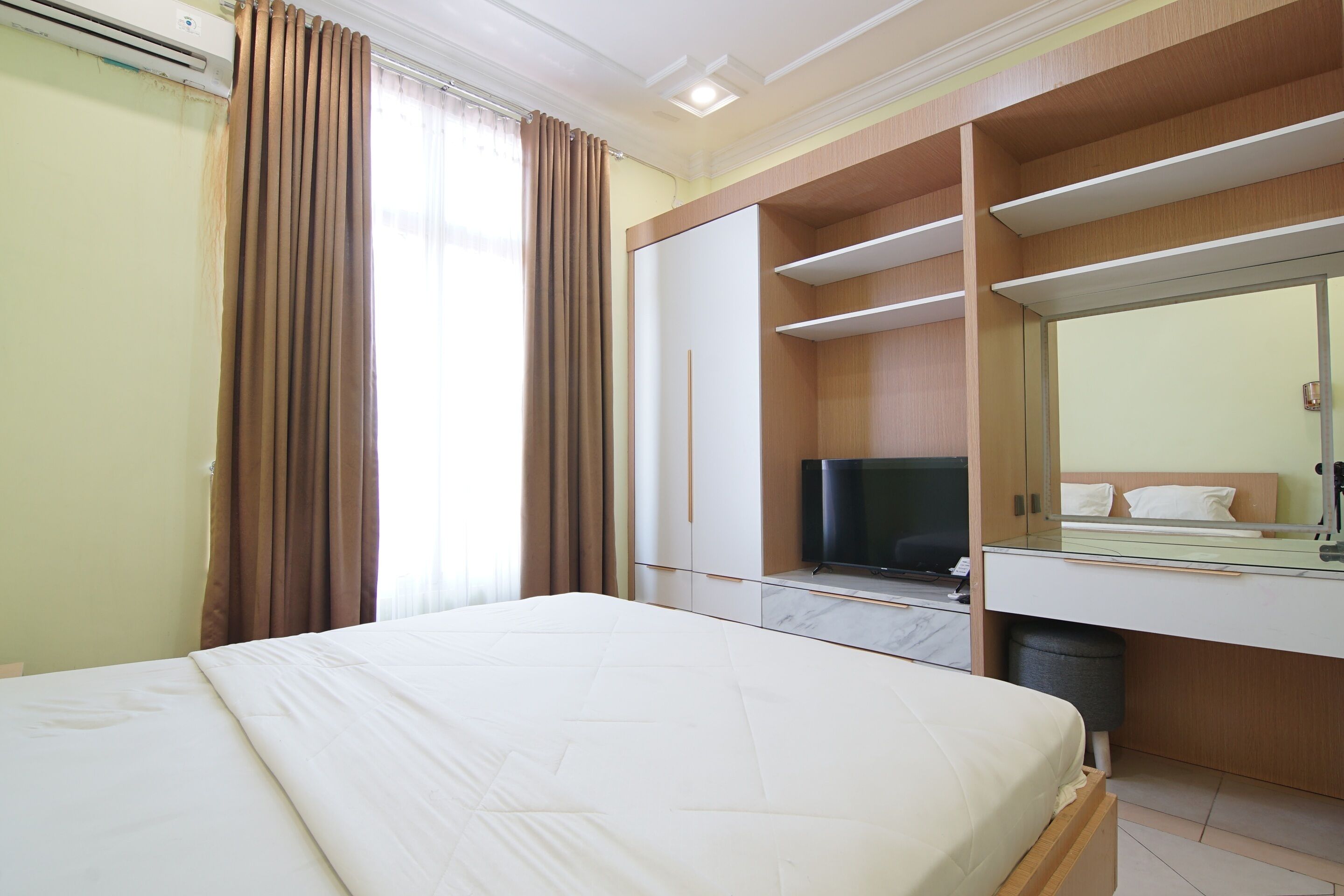 Habitación de hotel con cama, televisión, espejo y espacio de almacenamiento integrado.