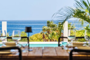 A dining table with chairs, a view of the ocean, and palm trees. - Vrbo Property (Kralendijk)