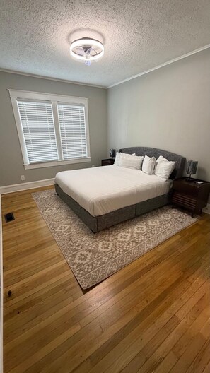 Un dormitorio con cama, mesita de noche, ventilador de techo y ventana con persianas.
