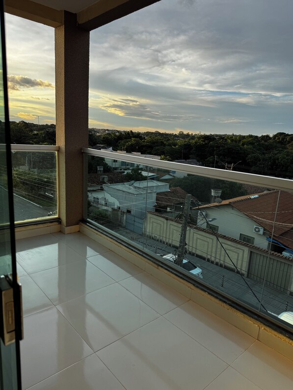 A balcony with a glass railing, a tiled floor, and a view of buildings and trees.