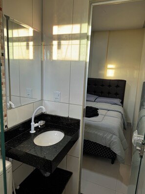 Une salle de bain moderne avec un lavabo blanc, un miroir et un plan de toilette noir.