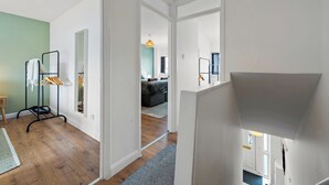 Un couloir avec un portant à vêtements, un escalier et, au fond, un salon.