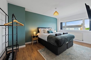 A bedroom with a bed, bedside table, lamp, and a view of the outside. - Cosy 3-Bed House Basildon | Contractors | Parking (Vange)