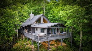 A cabin with a deck, large windows, and a hot tub. - NEW! Hidden Cabin with Mountain Views, Hot Tub, Fire Pit, Gameroom & More (Maggie Valley)