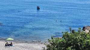A beach with rocky terrain, a boat in the water, and people swimming. - Impressive penthouse on the seafront (PEÑISCOLA)