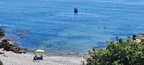 A beach with rocky terrain, a boat in the water, and people swimming. - Impressive penthouse on the seafront (PEÑISCOLA)