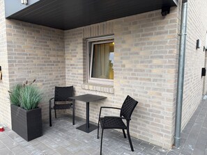Un patio con dos sillas, una mesa, un ventanal y un muro de ladrillo.