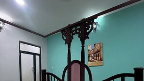 A room with a bed, a dining table, a chair, a wall with a painting, and a door.
