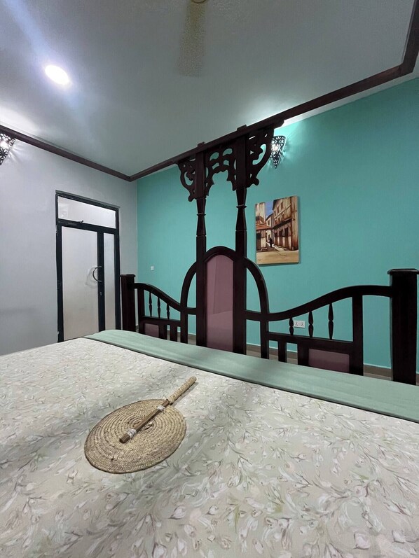 A room with a bed, a dining table, a chair, a wall with a painting, and a door. - Azure Chameleon House. (Jambiani)