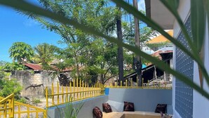 A balcony with a yellow railing, a seating area with cushions, and potted plants.