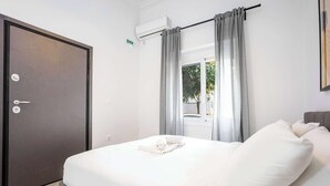 Una habitación de hotel con una cama, una puerta, una ventana con cortinas y un equipo de aire acondicionado.