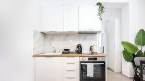 Una cocina moderna con armarios blancos, encimera de mármol, horno integrado y cafetera.