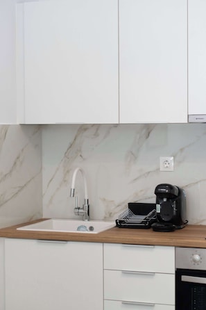 Una cocina con un lavamanos blanco, una cafetera Bosch y un salpicadero de mármol.