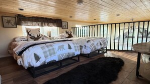 A bedroom with two beds, a black furry rug, wooden flooring, and a balcony with a railing.