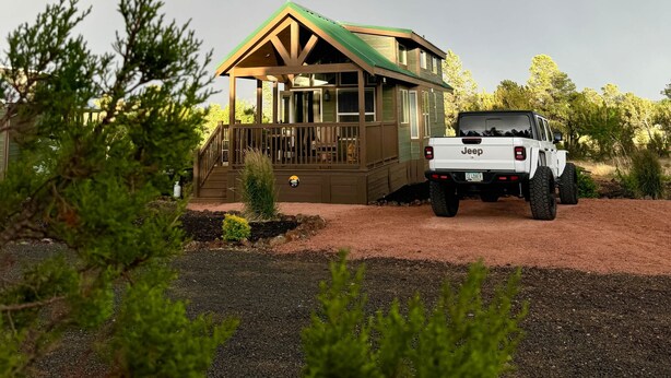 A house with a porch, a Jeep parked in front, and a rainbow in the sky.