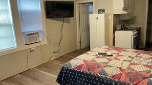 A bedroom with a bed, a television, a small kitchenette, and a door leading to another room. - Charming Efficiency Unit w/Cool AC in Aransas Pass (Aransas Pass)