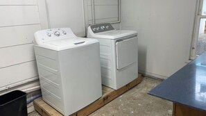 A laundry room with two stacked washers and dryers, a black trash bin, and a wooden floor. - Charming Efficiency Unit w/Cool AC in Aransas Pass (Aransas Pass)