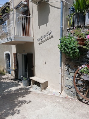 A building with a balcony, a stone wall, and a wooden cart with flowers. - Bisinchi village (village Bisinchi)