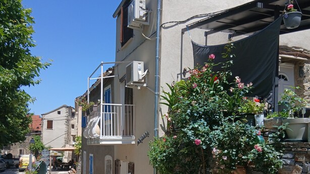 Eine enge Straße mit Gebäuden, einem Balkon mit Geländer und Pflanzkübeln.