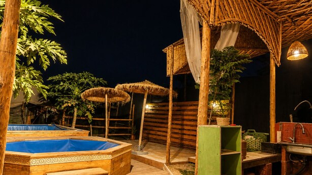 Una terrassa de fusta amb un banyera d'hidromassatge, una piscina petita i una zona de seients coberta amb ombrel·les.