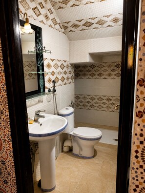 Een badkamer met twee wasbakken, een toilet en een douche. De wanden zijn betegeld met een patroon.