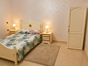 Een slaapkamer met een bed, twee nachtkastjes met lampen, een bijzettafeltje, een deur en een vloerkleed.