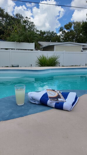 A poolside area with a glass of water, a towel, and a book. - House in Seminole with AC, close to beach, private pool, fenced yard for privacy (Seminole)