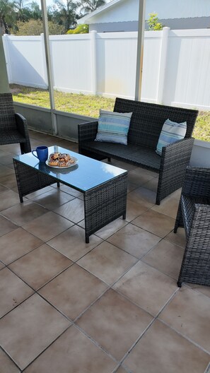 Un patio con mobiliario de mimbre, una mesa de vidrio y una bandeja de pasteles.