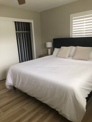 A bedroom with a bed, a nightstand, a lamp, a window with blinds, and a door with a striped pattern. - House in Seminole with AC, close to beach, private pool, fenced yard for privacy (Seminole)