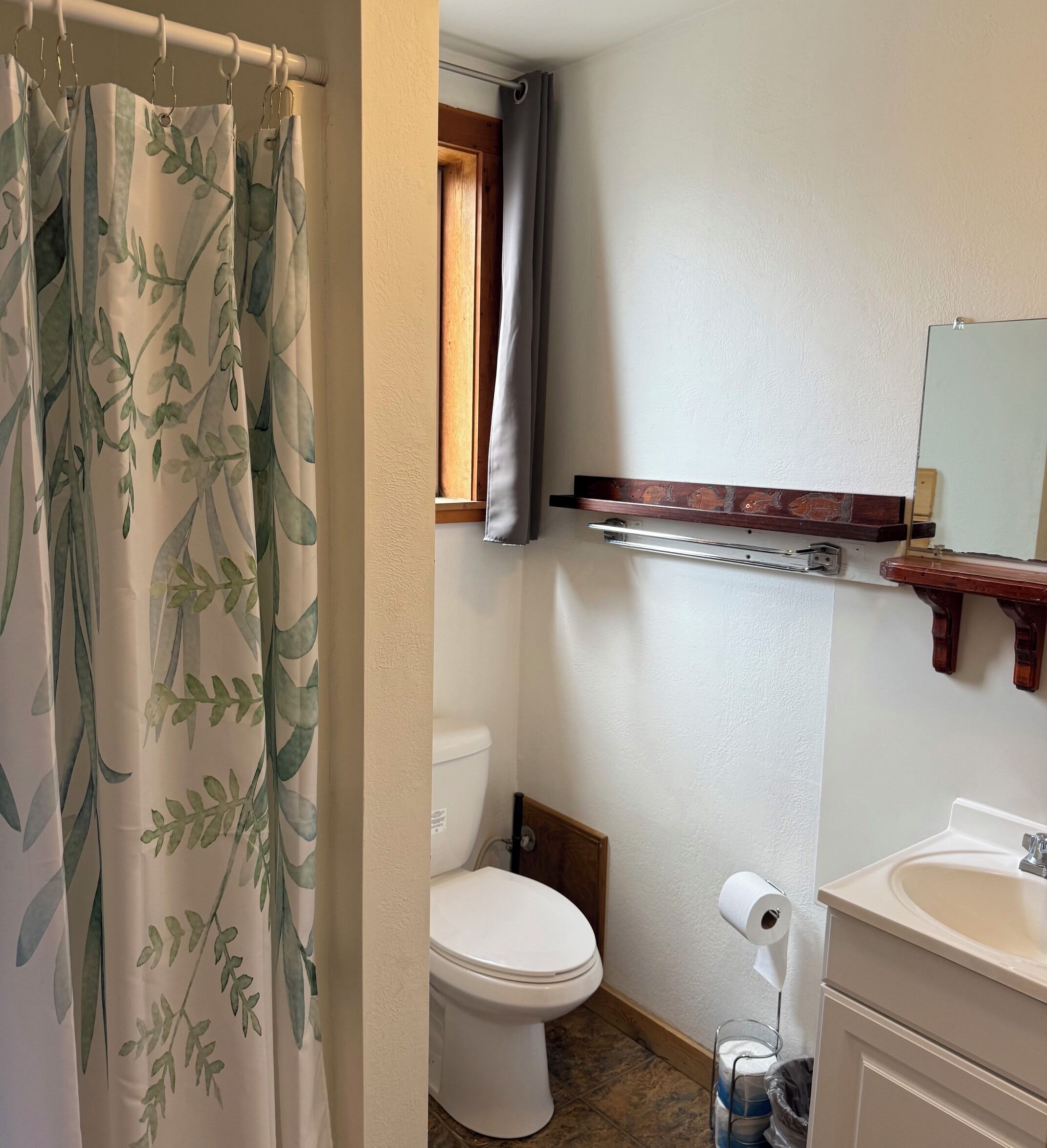 Un bagno con il water, una tenda da doccia, una finestra, uno specchio e un lavandino.