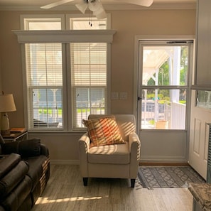 A living room with a sofa, armchair, and a fireplace. There are two large windows with blinds, a ceiling fan, and a door leading outside. - Cozy 1-bedroom mobile home in charming Leesburg 55+ community (Leesburg)